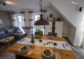 A dining area with a wooden table set for two, a sofa, and a staircase leading to an upper level.