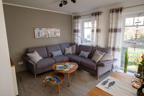 Uma sala de estar moderna com um sofá modular cinza, uma mesa de centro de madeira e uma grande janela com cortinas.