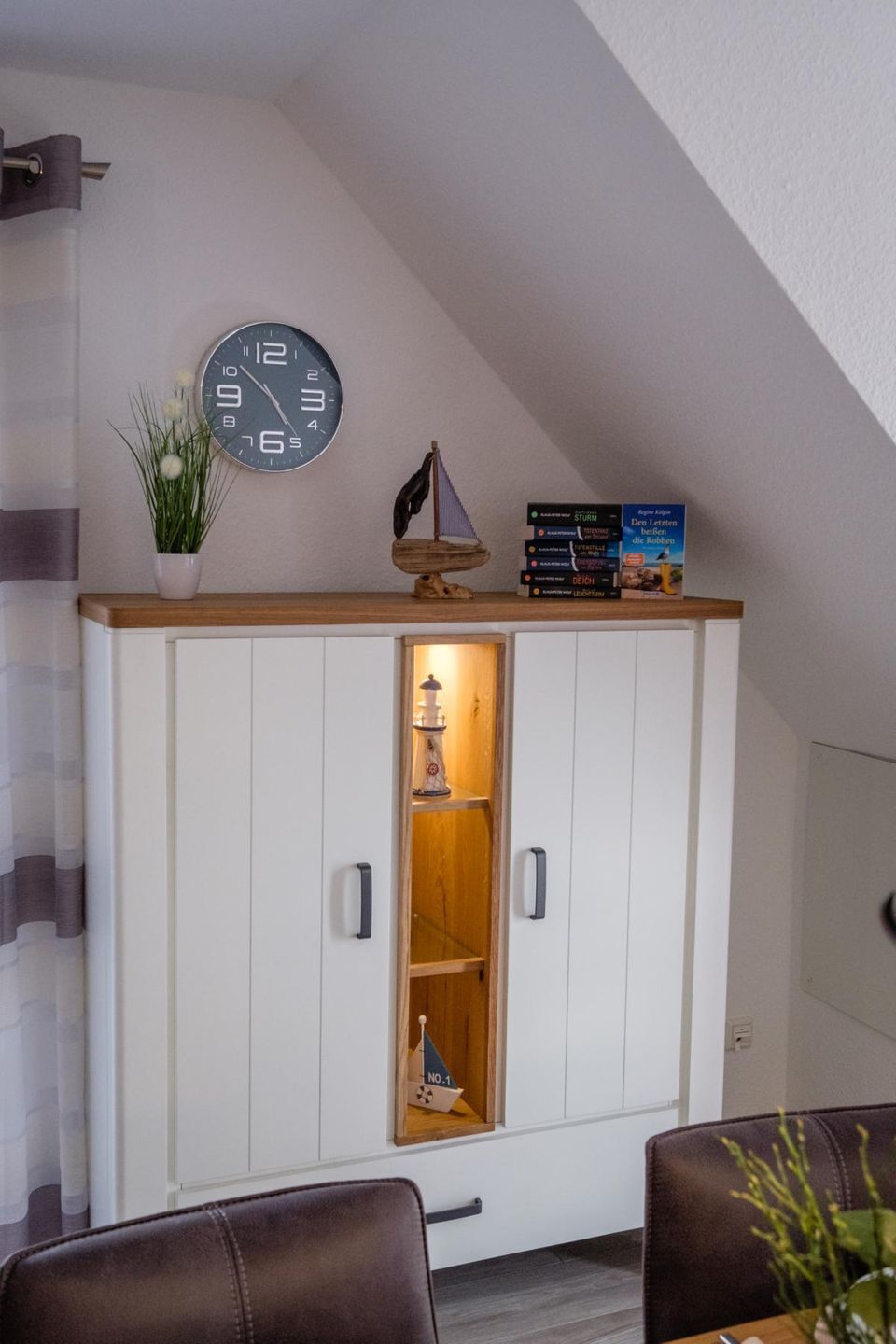 Ein Zimmer mit einem weißen Schrank, einer Uhr, einer kleinen Pflanze und einem Bücherregal.