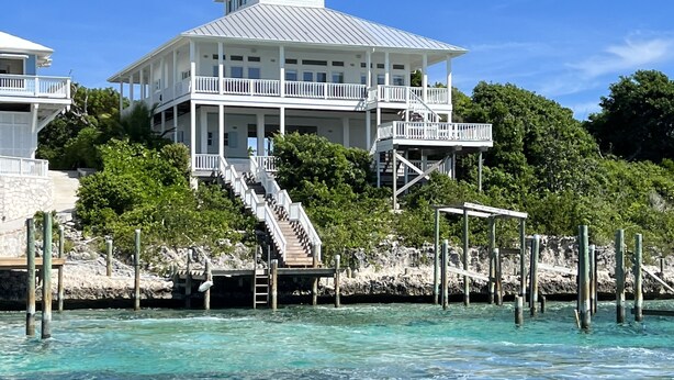 Une maison située sur la côte, dotée d’un grand balcon, d’un escalier menant à une terrasse, et offrant une vue sur l’océan.