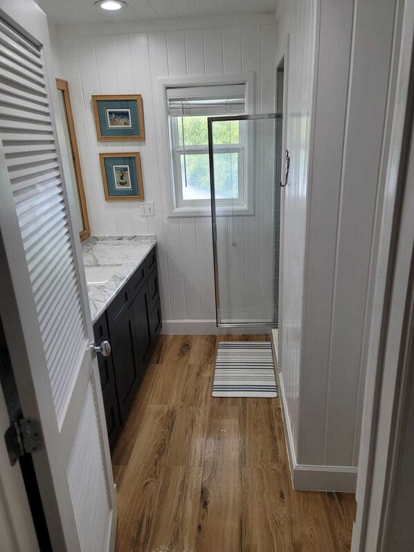 A kitchen with white cabinets, a marble countertop, and a window with blinds.