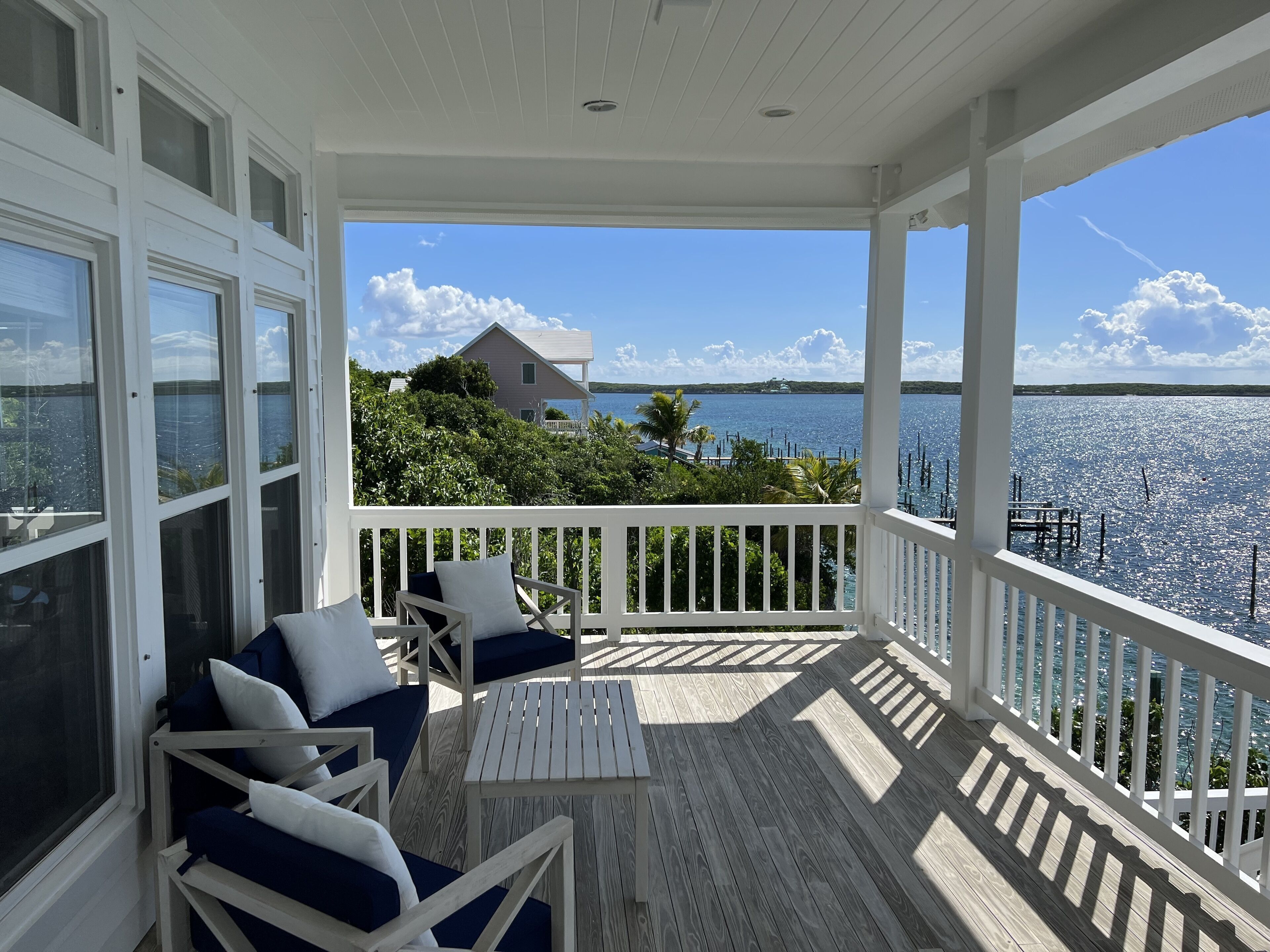 A covered outdoor area with a wooden deck, white railings, and a view of a house and water.
