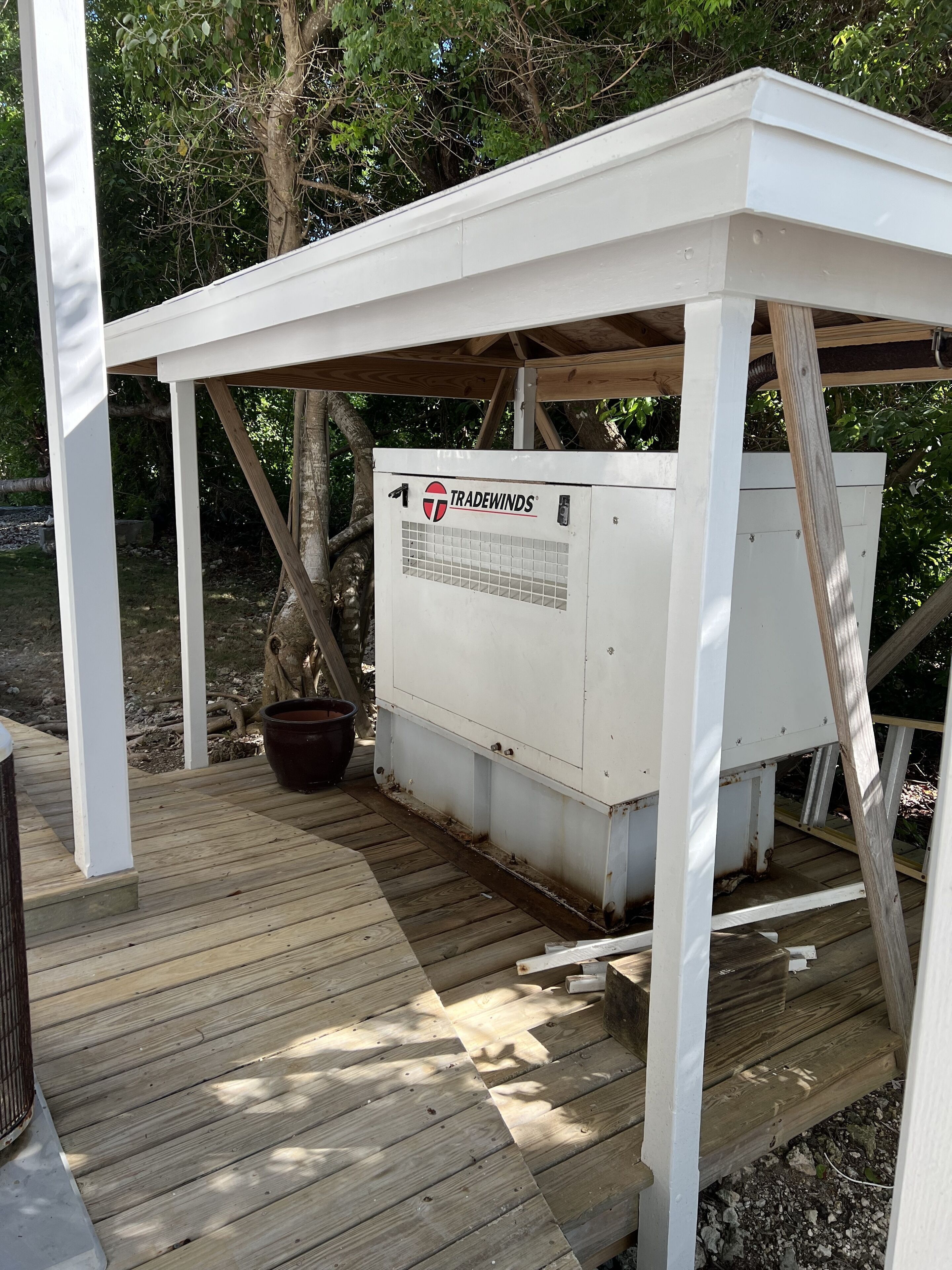 Een witte buitenconstructie met een geïnstalleerde airconditioning unit, genaamd “Tradewinds”, op een houten terras.