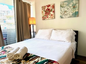 Une chambre d’hôtel avec un lit, deux oreillers, une serviette roulée, une lampe et deux tableaux aux motifs floraux accrochés au mur.