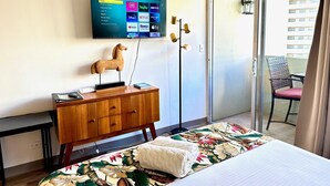 Une chambre d’hôtel avec un lit, une commode en bois, un téléviseur fixé au mur diffusant des services de streaming, une sculpture équestre décorative et une vue sur un bâtiment à travers une porte vitrée.