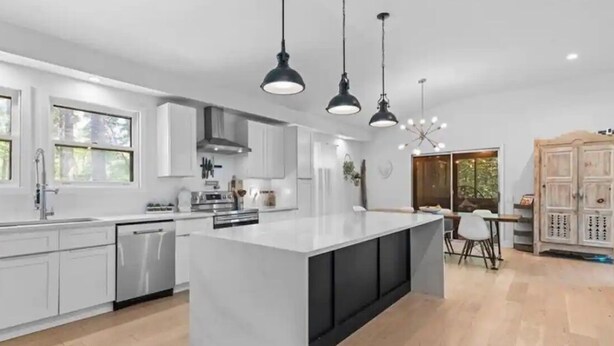 Een moderne keuken met witte kastjes, een centraal eiland en hanglampen.