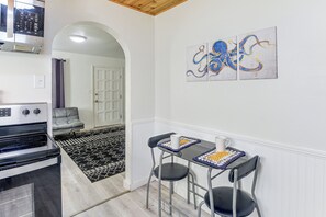 Een compacte keuken met een inbouwoven, een eethoek met tafel en stoelen, en een gang die leidt naar een slaapkamer.