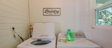 Une buanderie avec un panneau indiquant qu’elle est en libre-service, un lave-linge, un sèche-linge et une fenêtre donnant sur des arbres.