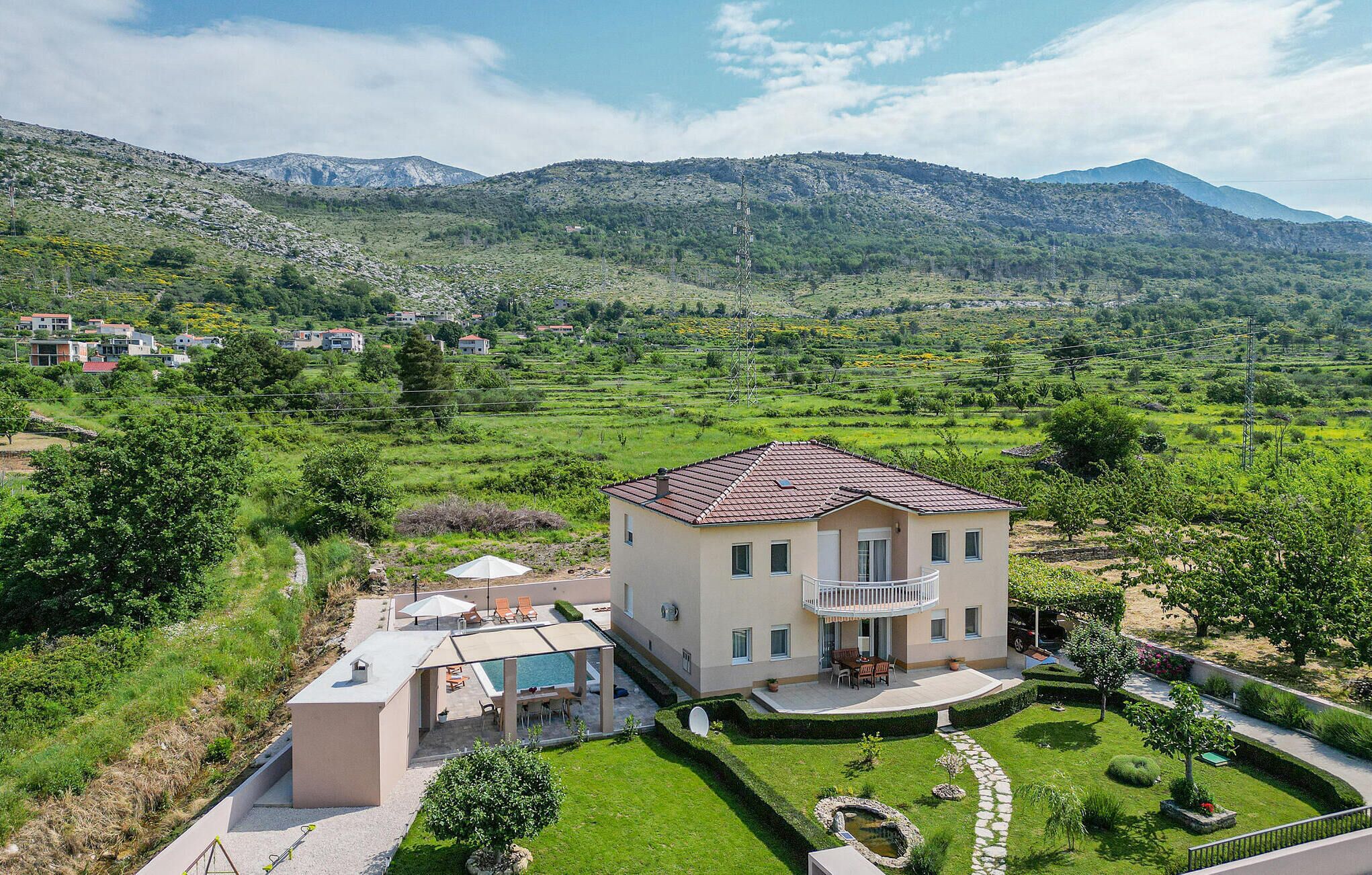 A two-story house with a balcony, a swimming pool, and a well-maintained garden.