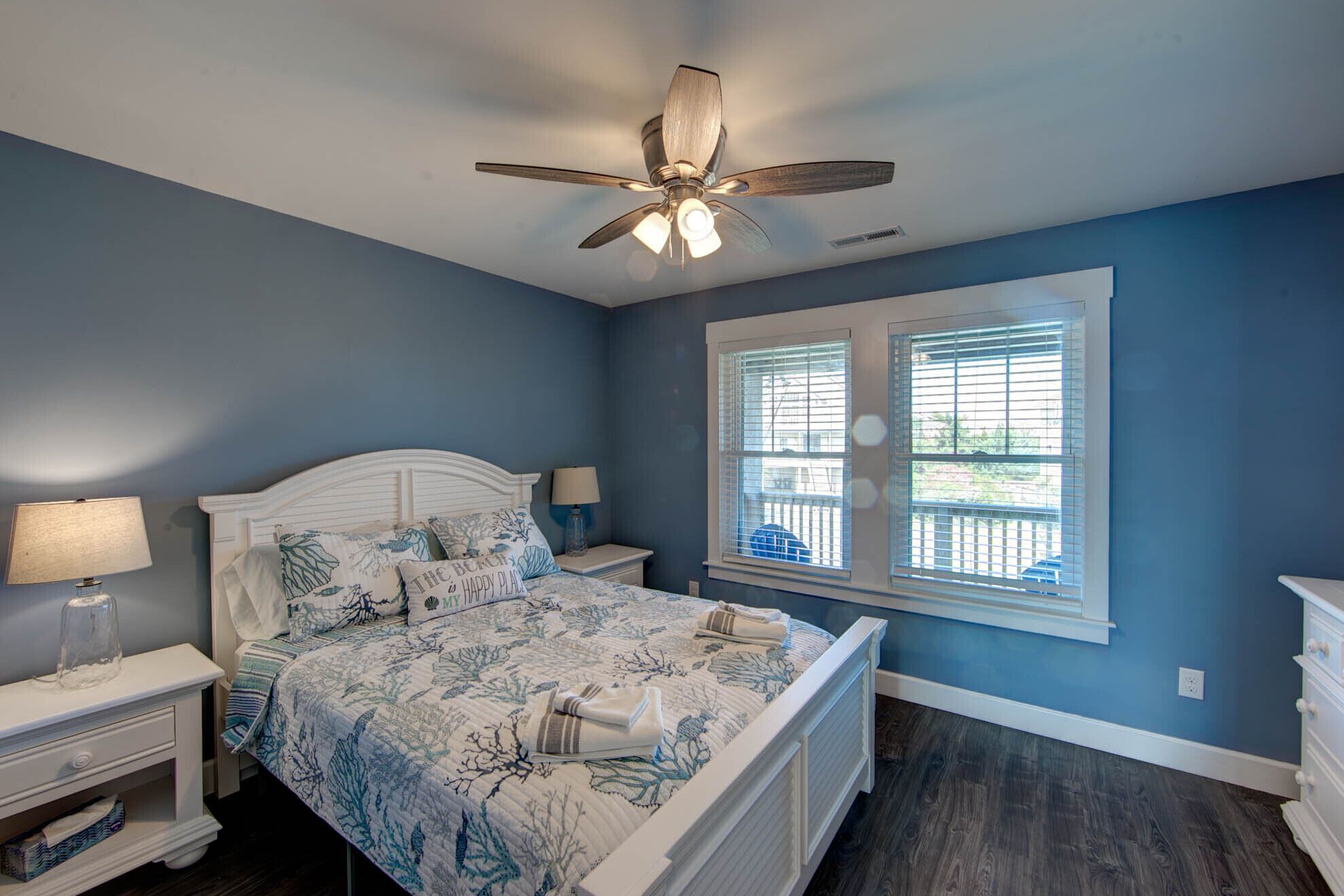 A bedroom with a bed, nightstands, a ceiling fan, and a window with blinds.