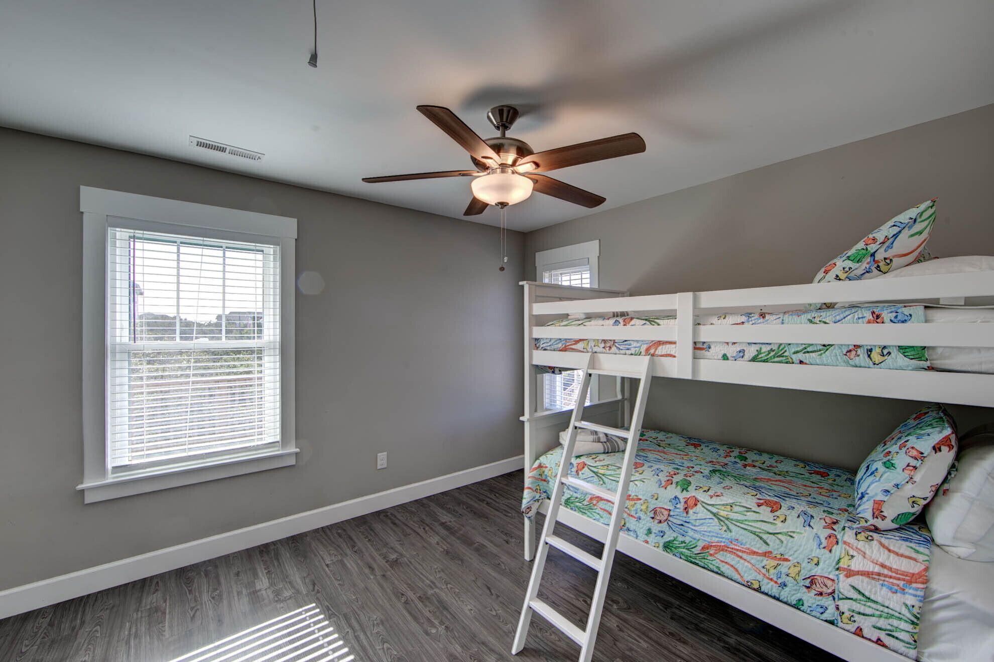 Une chambre d’enfant avec un lit superposé, un ventilateur de plafond, une fenêtre avec des stores et une vue sur l’extérieur.