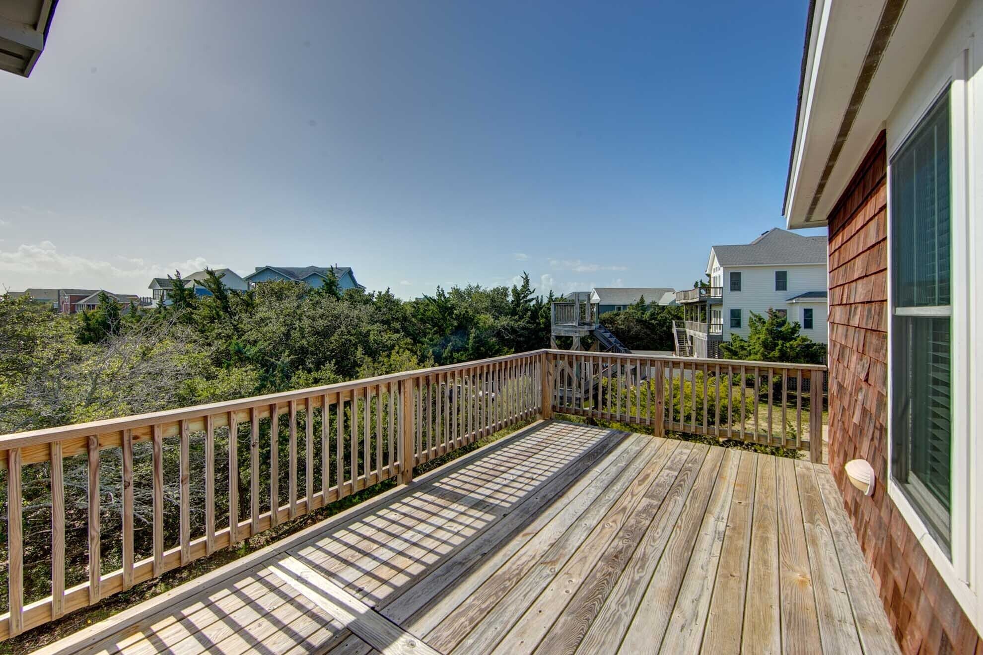A wooden deck with a railing, overlooking a residential area with houses and dense vegetation.