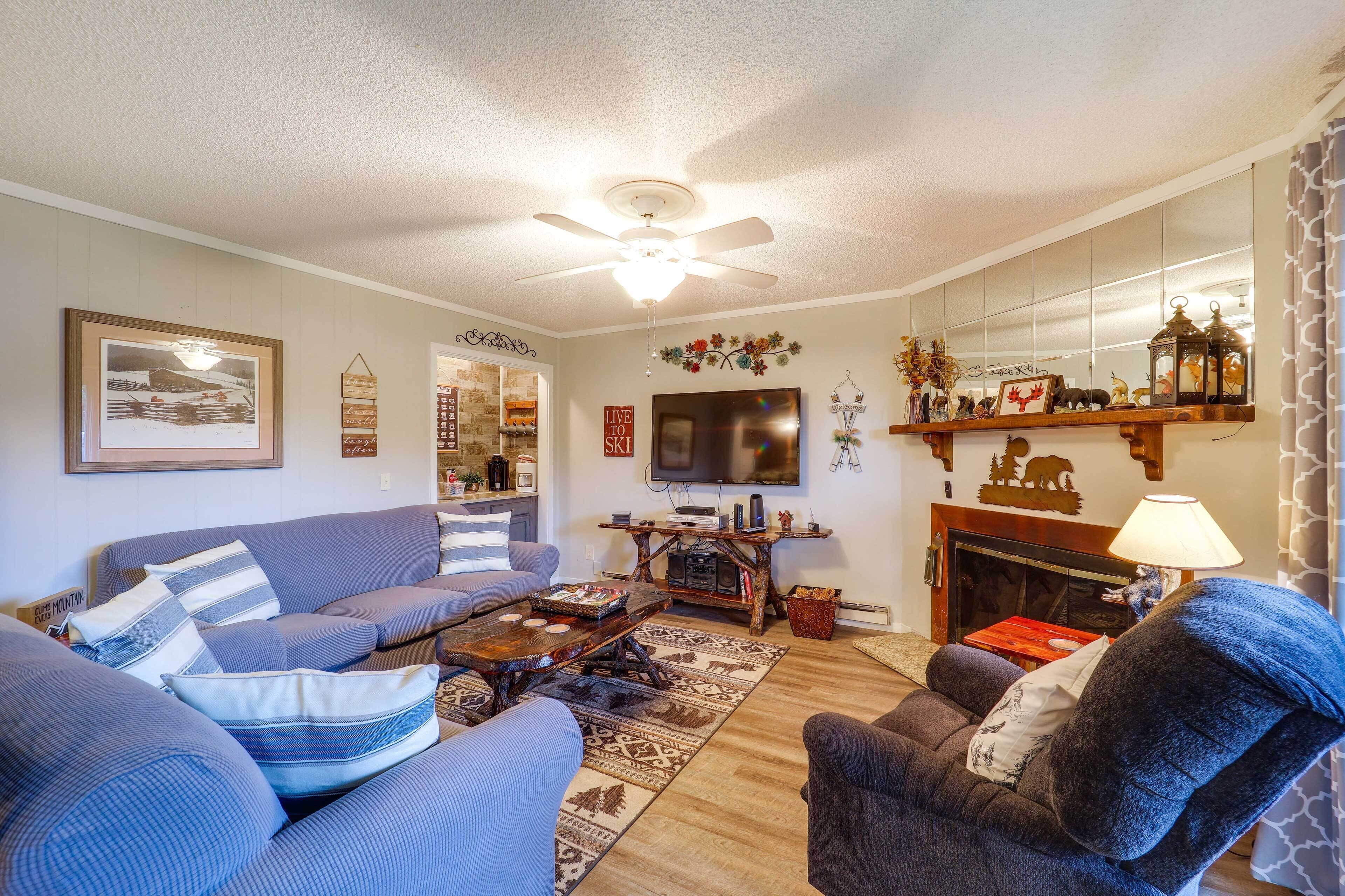 Un salon comprenant un canapé, un fauteuil, une table basse, une cheminée, un téléviseur et des objets de décoration.