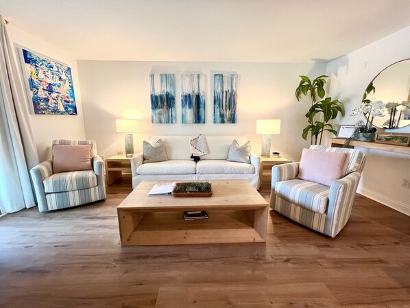 A living room with a sofa, two armchairs, a coffee table, and a painting on the wall. - Chic Oasis by Sandpiper | Near Beach (Seabrook Island)