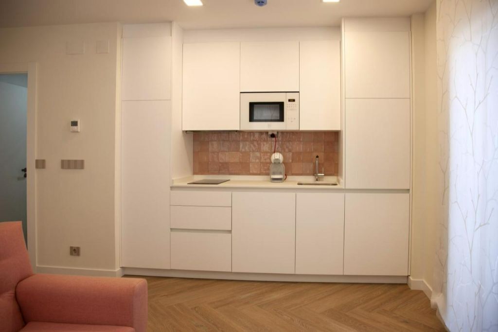 Una cocina compacta con armarios blancos, un microondas y un lavamanos.