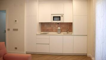 Una cocina compacta con armarios blancos, un microondas y un lavamanos.