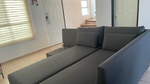 Ein modernes Wohnzimmer mit einem grauen Sofa, einem kleinen Tisch und einem Fenster mit Jalousien.