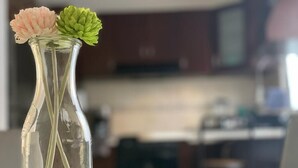 Eine klare Glasvase mit zwei Blumen auf einem Tisch in einem Raum, der unscharf im Hintergrund wirkt.