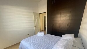 Ein Schlafzimmer mit einem Bett, weißer Bettwäsche, einem dunklen Kleiderschrank und einer Tür zu einem anderen Raum.