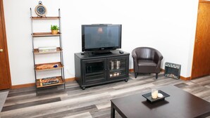A living room with a TV on a stand, a bookshelf, a leather chair, and a coffee table. - 2 Bedroom, 1 Bathroom Convenient Green Bay Getaway (Bellevue)