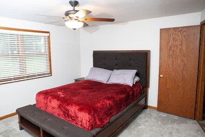 A bedroom with a bed, a ceiling fan, a wooden door, and a window with blinds.