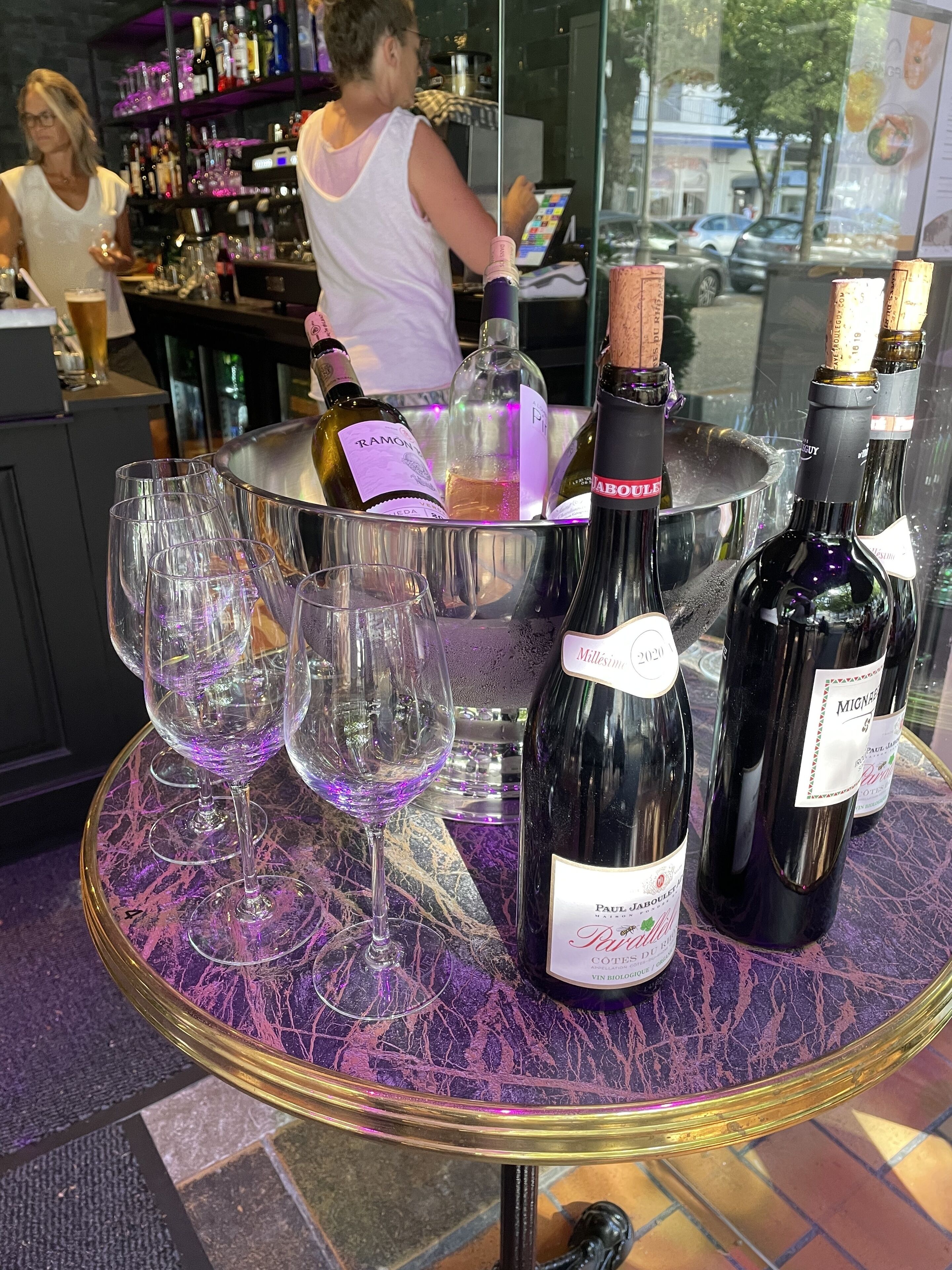Zona de bar con una mesa redonda que muestra botellas de vino y copas.