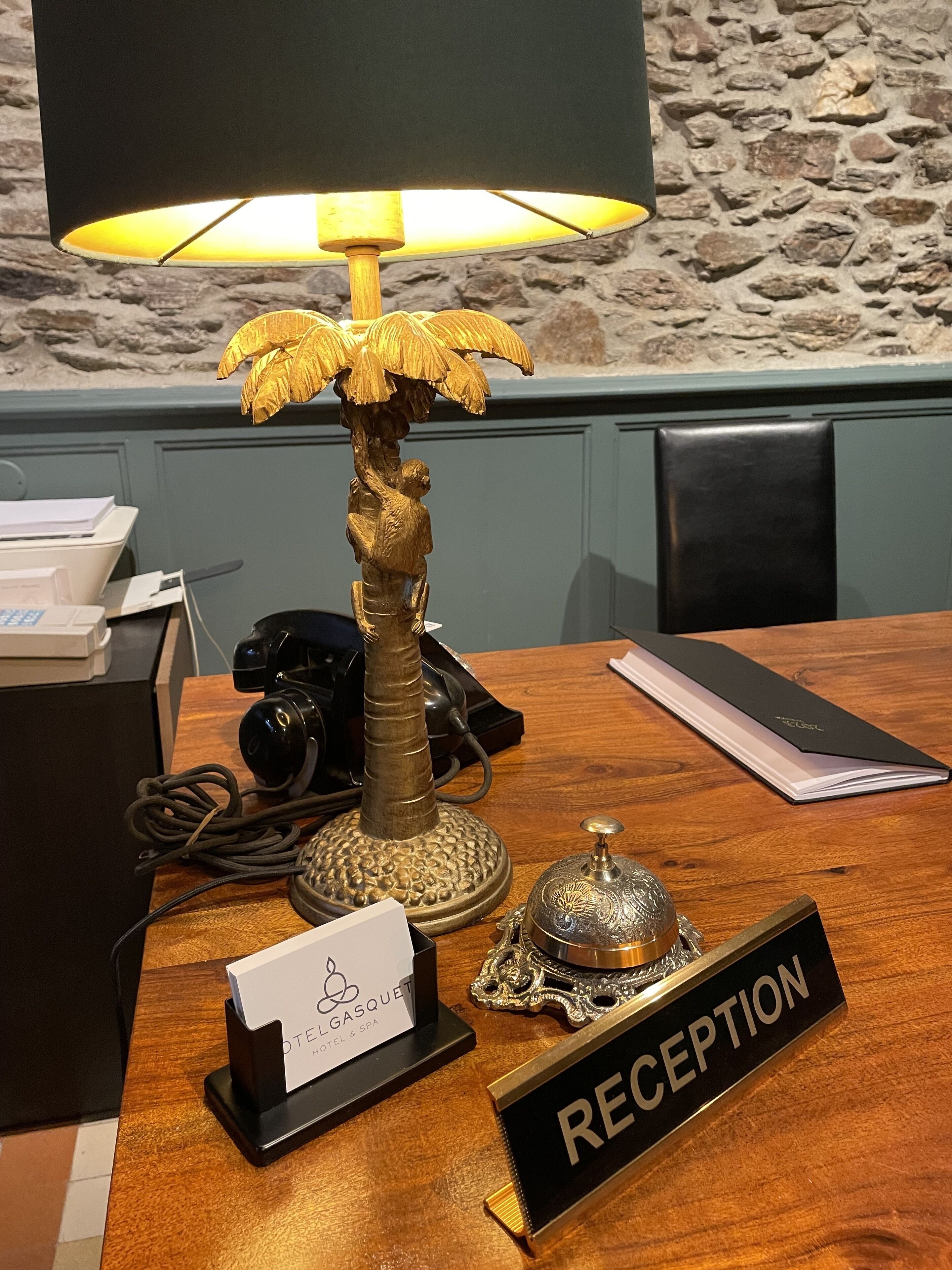 Balcão de recepção com luminária, porta-cartões com nomes, placa de recepção e telefone.