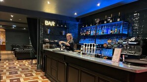 Zona de bar con un bartender, estantes llenos de licores y un suelo con diseño.
