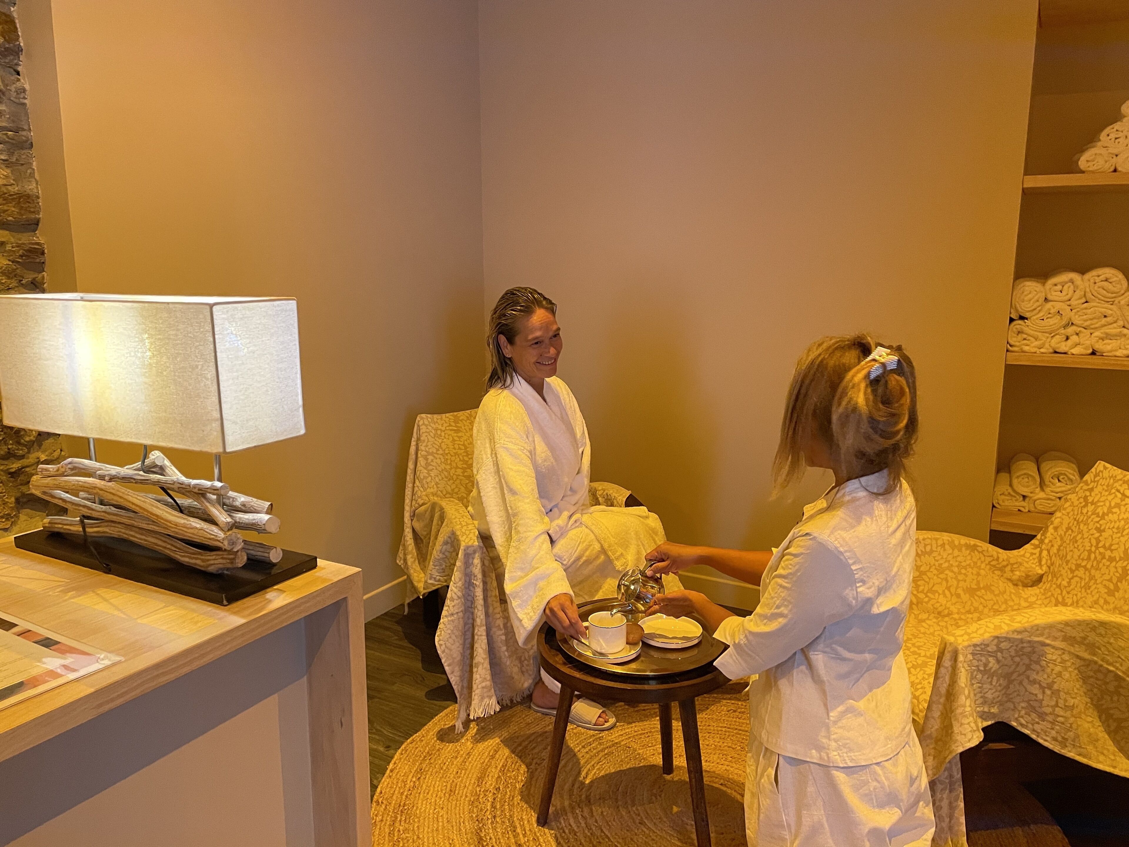 A hotel room with a wooden side table, a lamp, and a bed with a white cover.