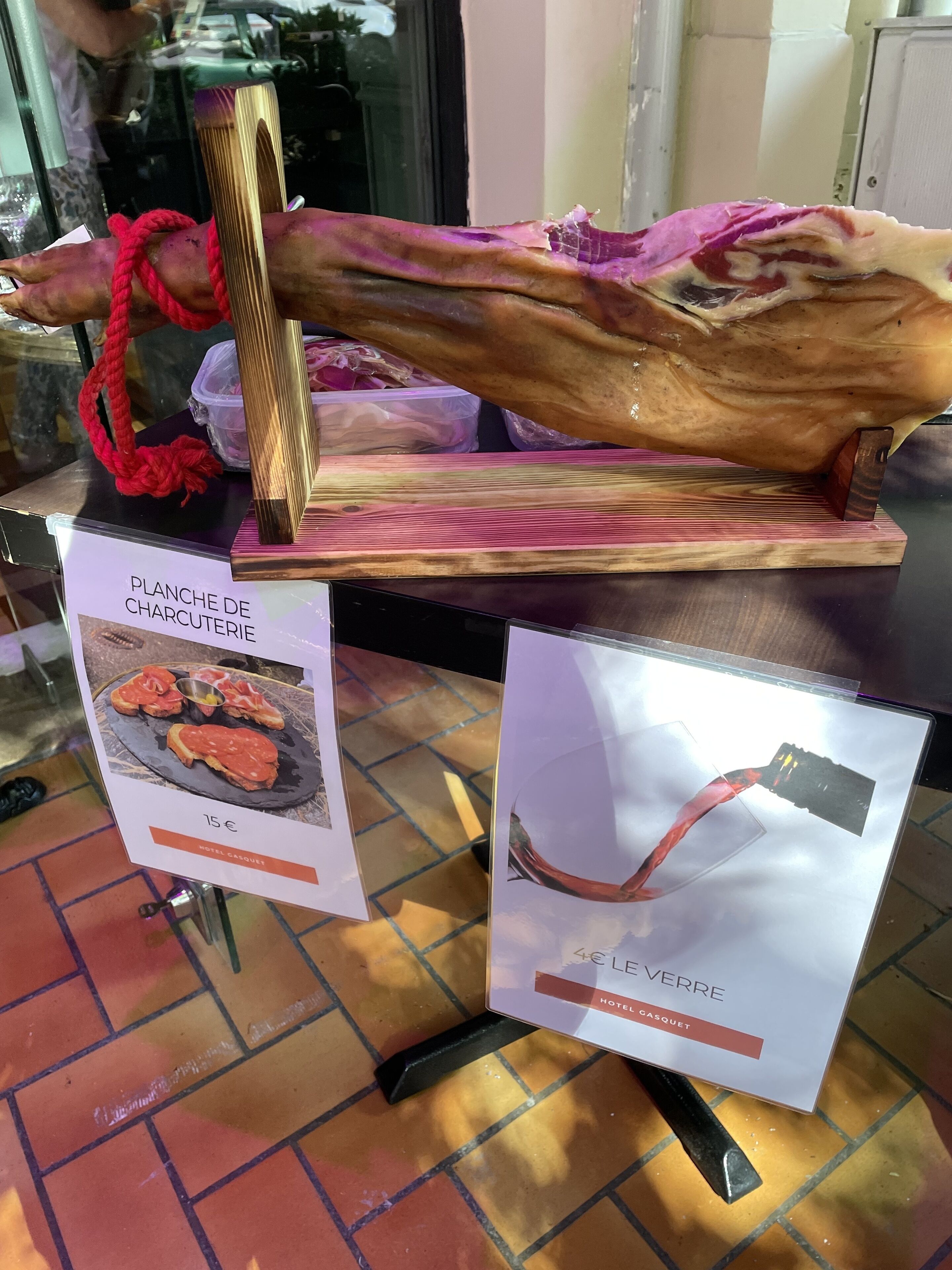 Un cochon entier, rôti et exposé sur un présentoir en bois, avec des panneaux indiquant « PLATEAU DE CHARCUTERIE » et « LE VERRE », ainsi que les prix.
