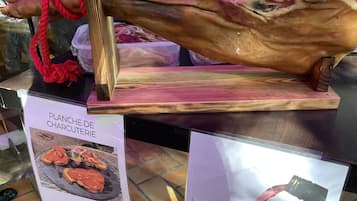 Un cochon entier, rôti et exposé sur un présentoir en bois, avec des panneaux indiquant « PLATEAU DE CHARCUTERIE » et « LE VERRE », ainsi que les prix.