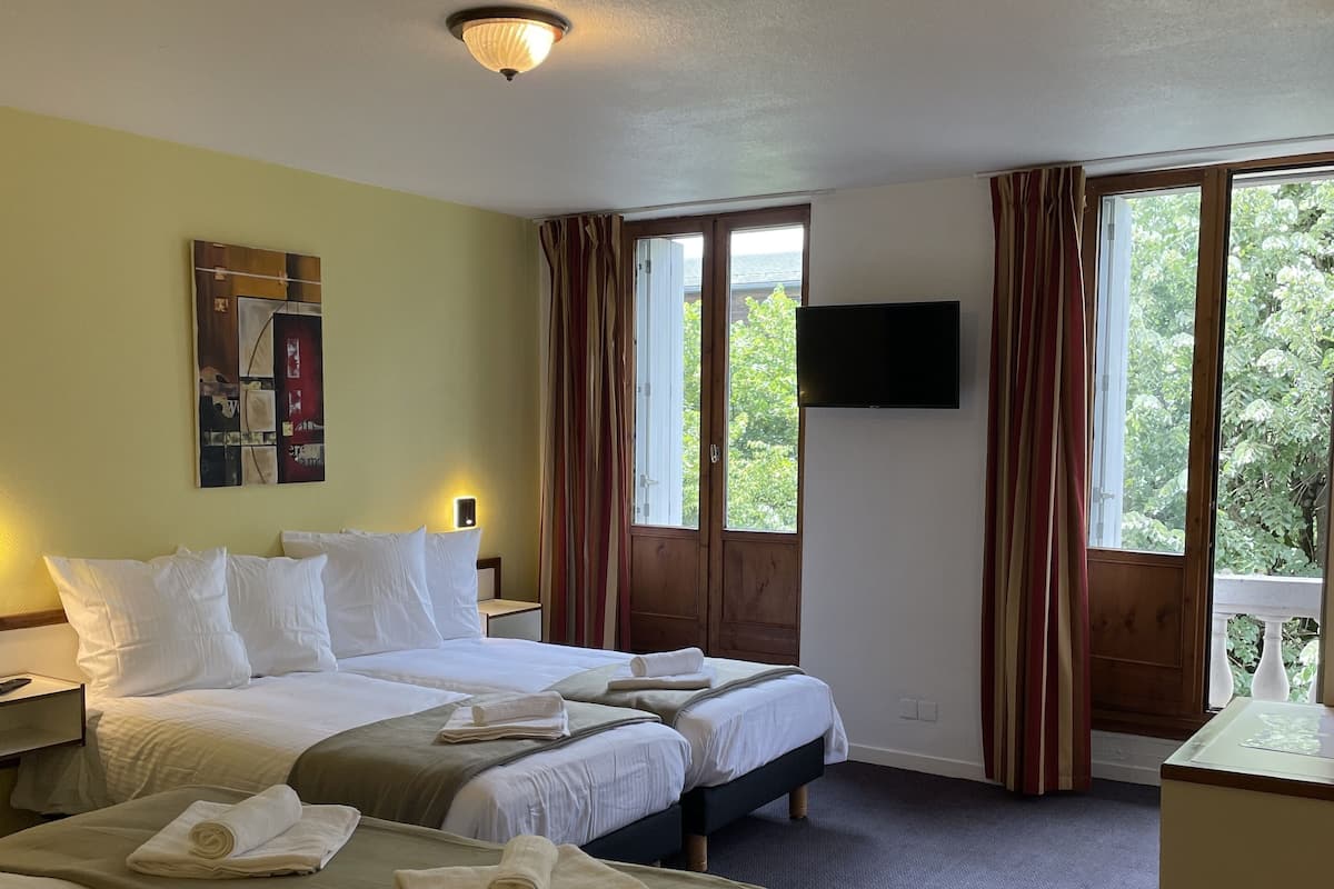 Habitación de hotel con dos camas, un televisor de pantalla plana y ventanas amplias con cortinas.
