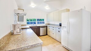 A modern kitchen with white cabinets, a granite countertop, a built-in dishwasher, and a large refrigerator.