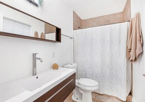 Une salle de bain avec un lavabo blanc, un miroir, des toilettes et un rideau de douche.