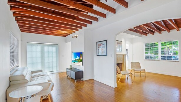 A spacious living room with wooden beams, a white couch, a dining table, and a TV.