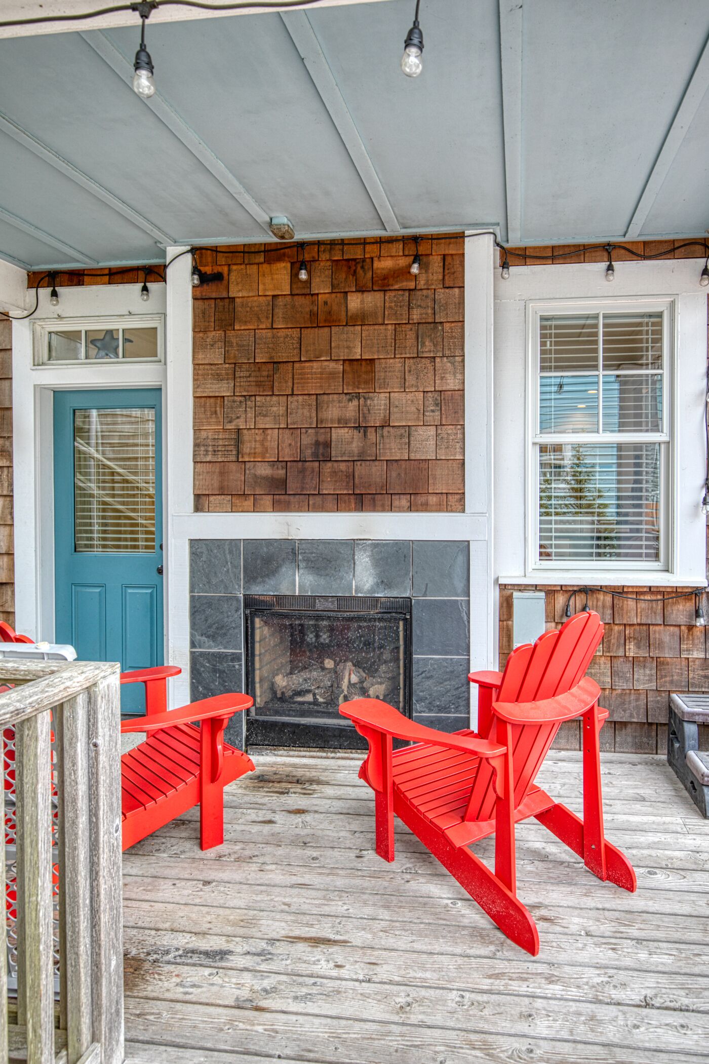 A covered porch with a fireplace, red Adirondack chairs, and a blue door.