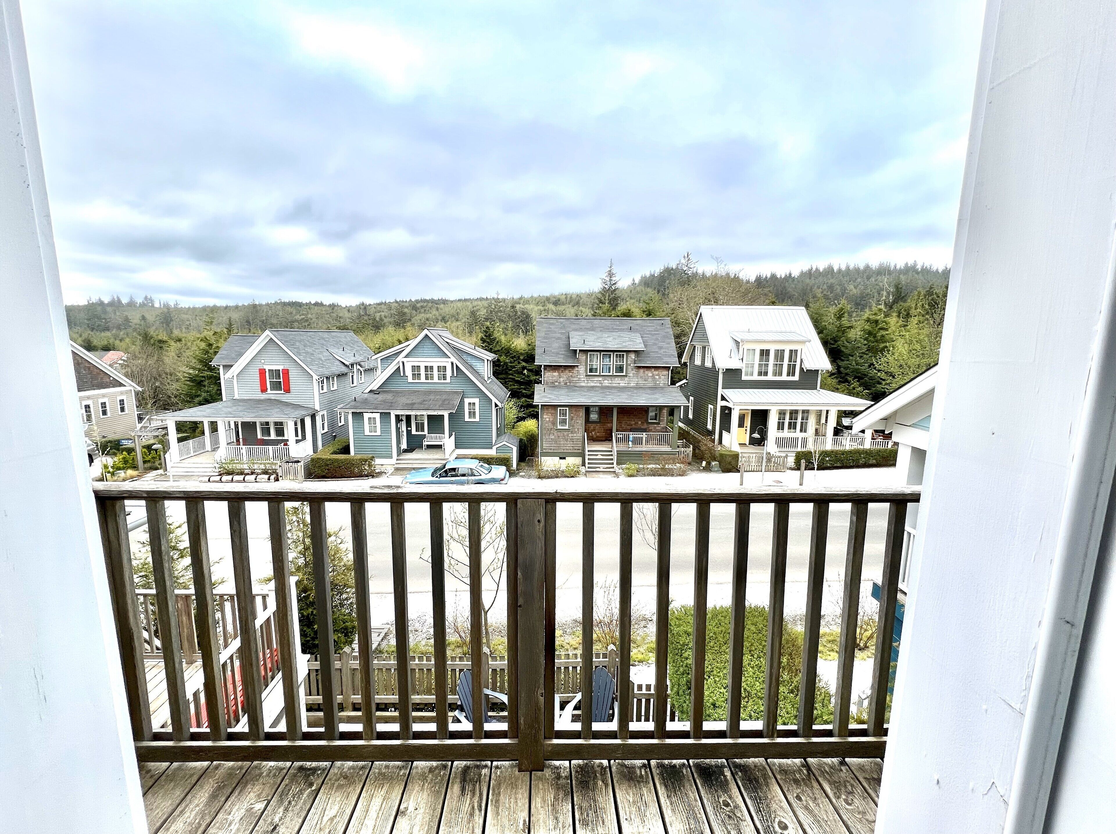 A wooden deck with a view of several houses and a forested hillside.