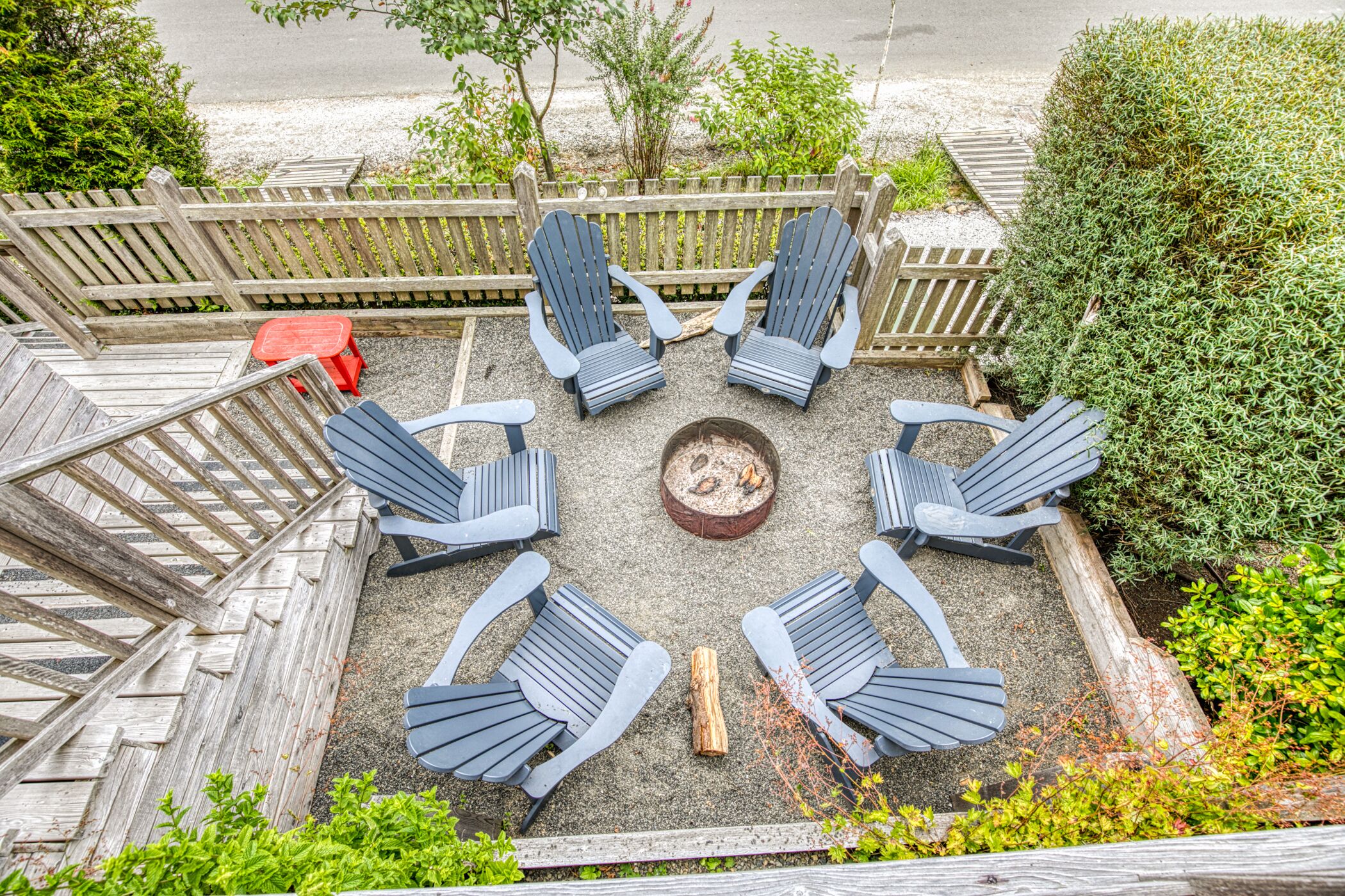 A circular outdoor seating area with six Adirondack chairs around a central fire pit.