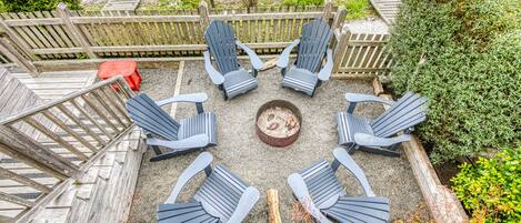 A circular outdoor seating area with six Adirondack chairs around a central fire pit.