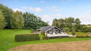 A small, single-story cabin with a sloped roof, surrounded by a well-maintained lawn and dense trees. - Lovely home in Roslev with WiFi (Roslev)
