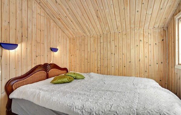 Une pièce aux murs lambrissés, avec un lit, deux lampes fixées au mur et une fenêtre.
