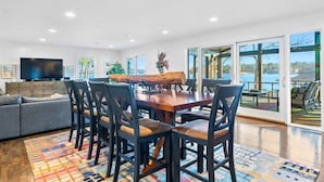 A spacious living area with a large wooden table, comfortable seating, a flat-screen TV, and a view of the outdoors. - Peaceful Lakeside | Stunning Views | Private Dock (Hot Springs)