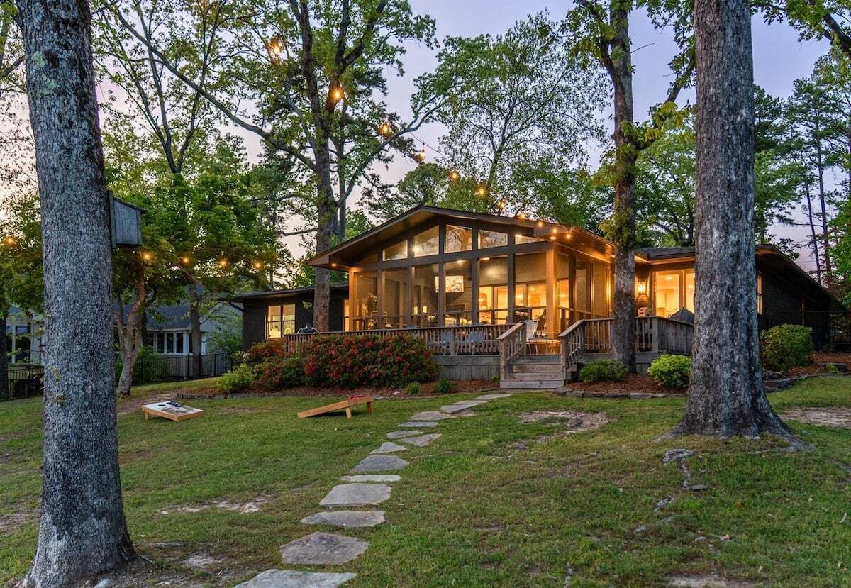 Une maison dotée d’une grande façade vitrée, d’une terrasse en bois et d’un chemin de pierre menant à l’entrée.