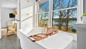 A modern bathroom with a bathtub, a wooden tray, and a view of a lake through large windows. - Peaceful Lakeside | Stunning Views | Private Dock (Hot Springs)