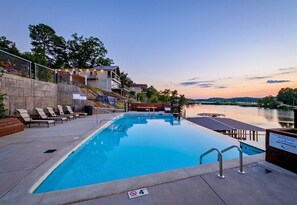 Une piscine avec des chaises longues, une terrasse en bois et une vue sur un lac au crépuscule.
