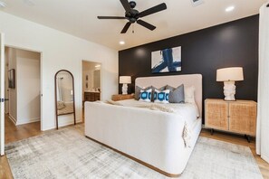Une chambre à coucher avec un lit, un ventilateur de plafond, des lampes de chevet et un grand tableau abstrait accroché au mur.