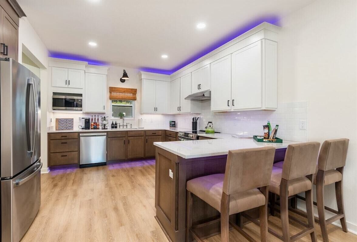 A modern kitchen with white cabinets, a stainless steel refrigerator, a dishwasher, and a central island with bar stools.