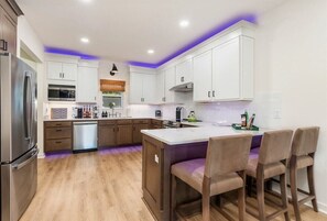 A modern kitchen with white cabinets, a stainless steel refrigerator, a dishwasher, and a central island with bar stools.