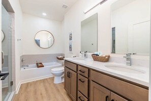 Une salle de bain moderne avec une baignoire, deux lavabos, des toilettes et un grand miroir.