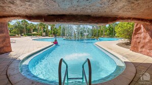 A swimming pool with a water fountain, surrounded by palm trees and a stone archway. - KonaKai-Sandestin® 2BR/2.5BA Views-Walk to Beach! (Miramar Beach)